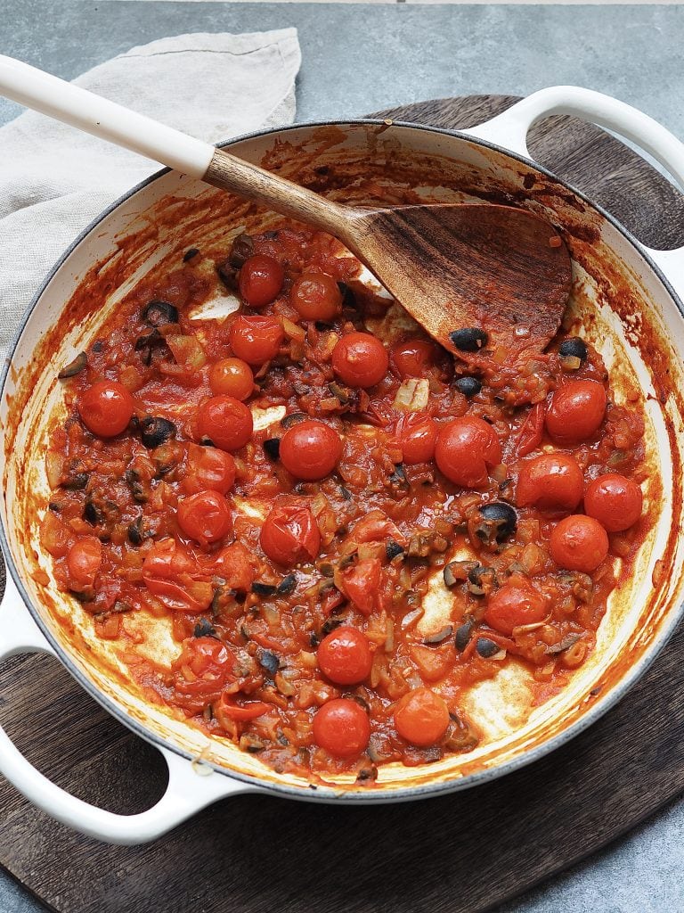 Stirring cherry tomatoes into a pan of onions.