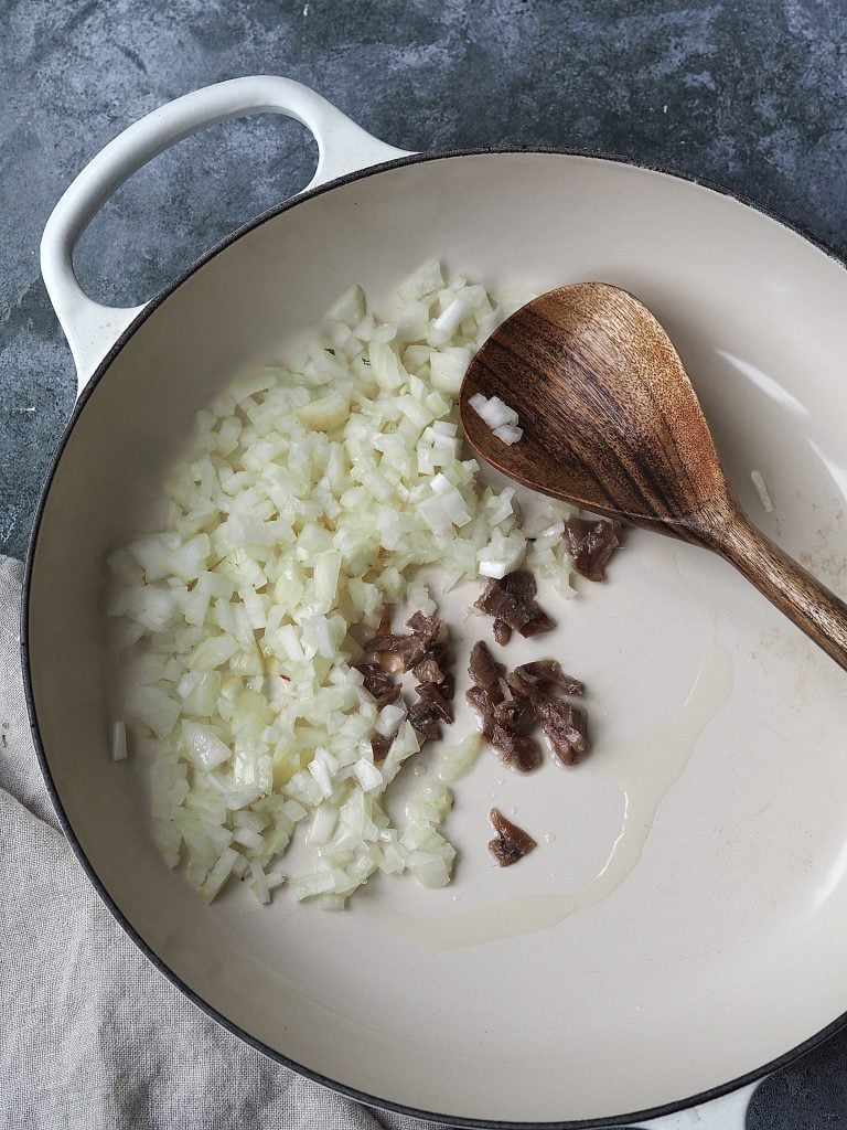 Onions and anchovies being fried in a shallow casserole dish.