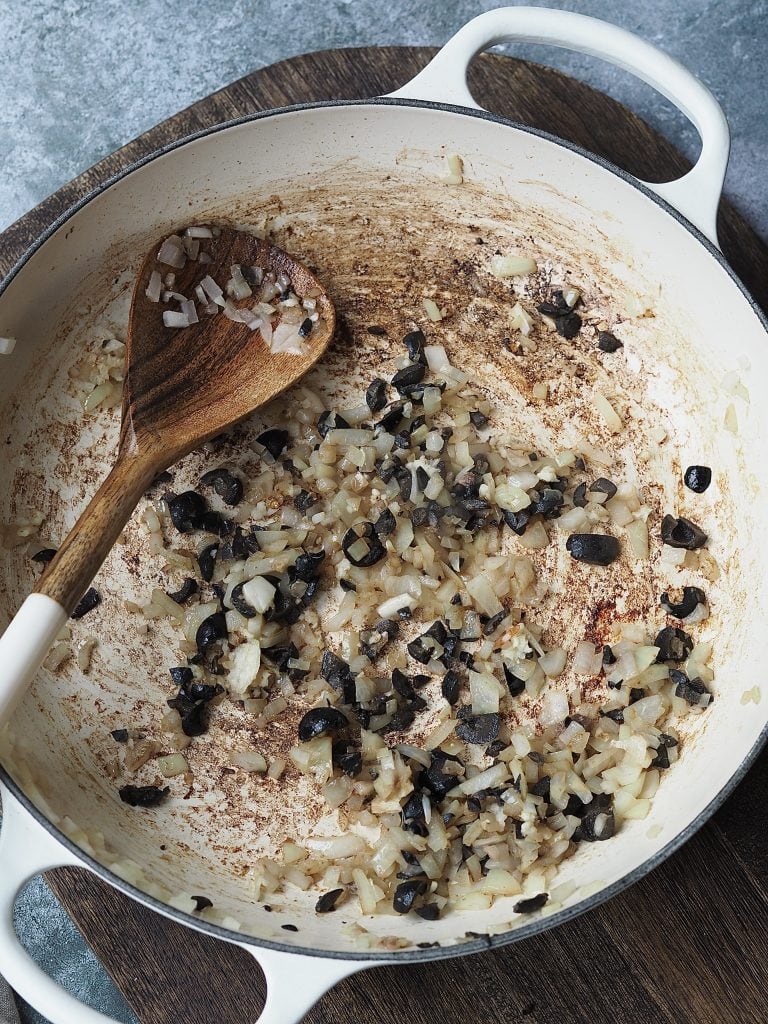 Frying onions, anchovies and chopped black olives in a shallow casserole dish.