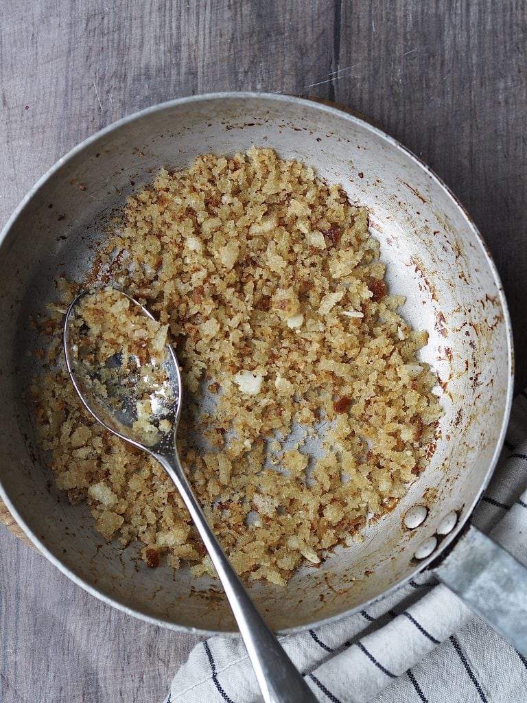 Breadcrumbs toasting in a metal frying pan.