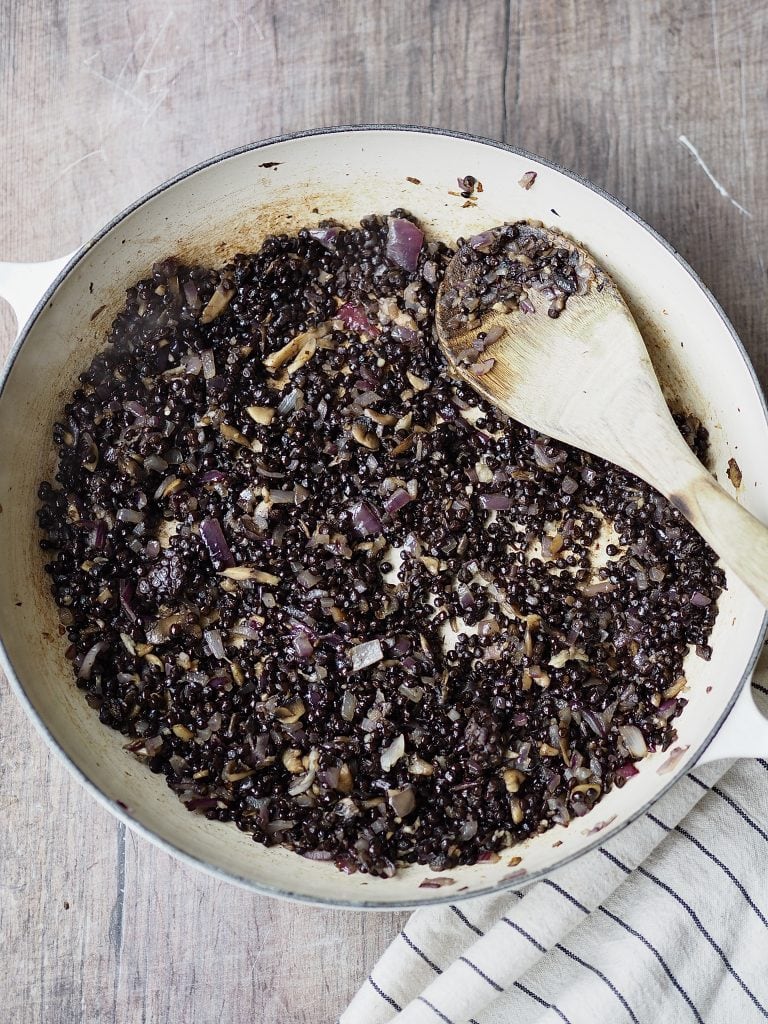 Lentils being stirred into a shallow casserole dish. 