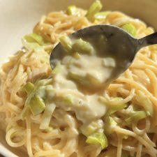 spooning sauce over leek pasta with a spoon in a white bowl