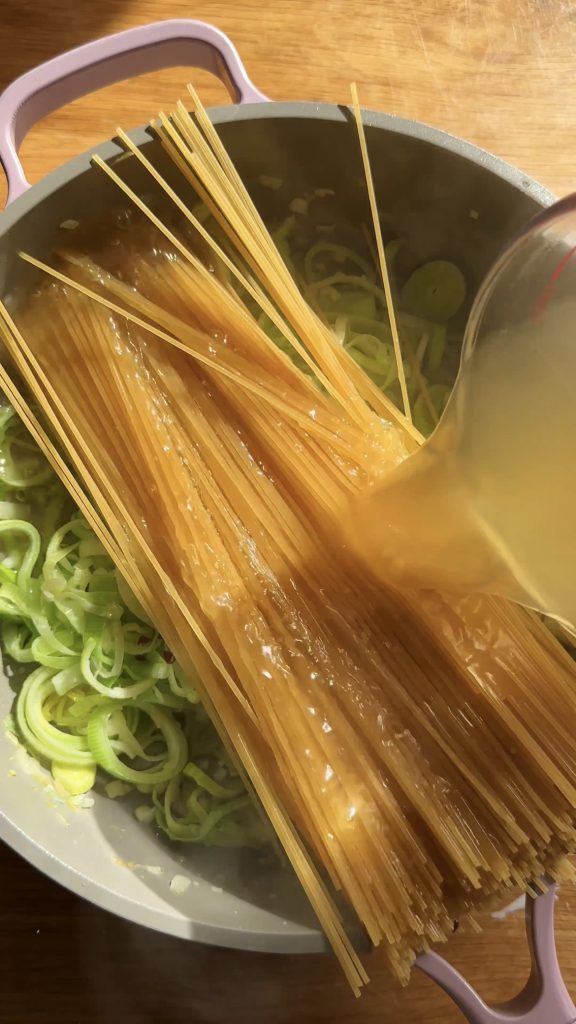 adding stock to pasta in a large saucepan