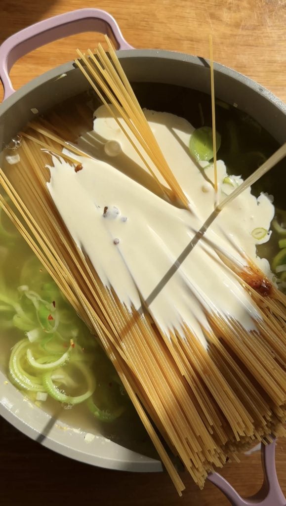 adding cream to pasta in a large saucepan