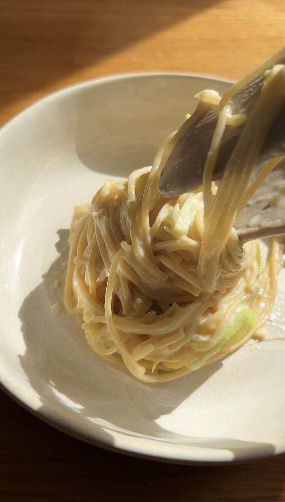 adding leek pasta to a beige bowl with tongs