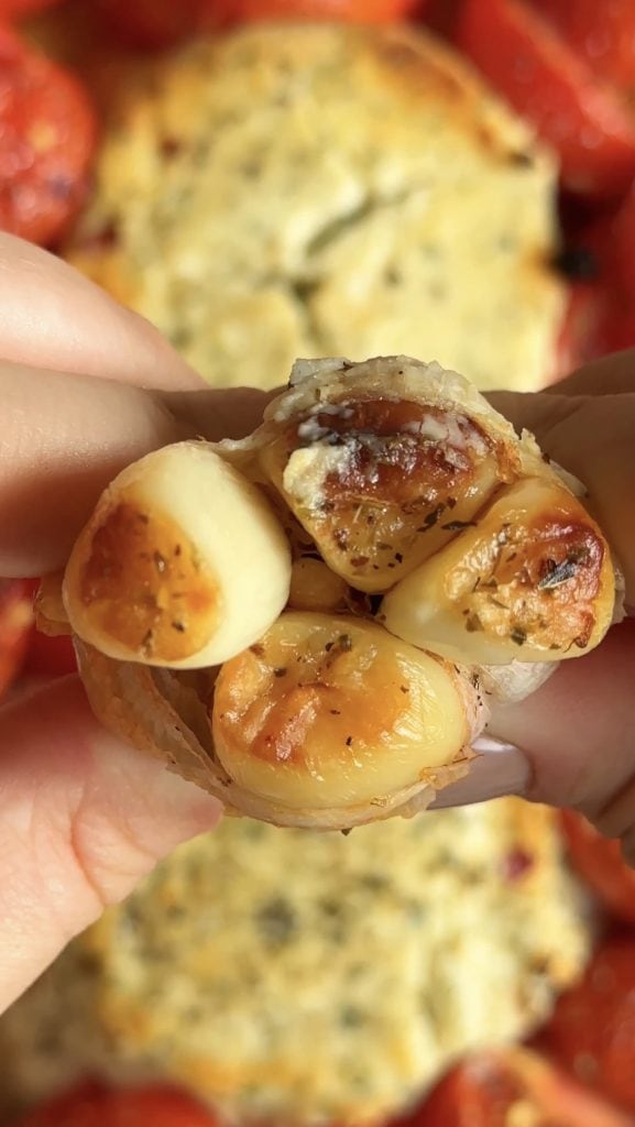 woman squeezing a head of roasted garlic to pop out the bulbs