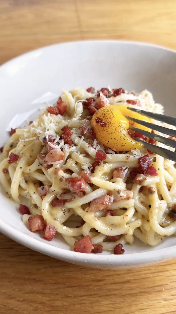 breaking the egg yolk with a fork on the udon carbonara