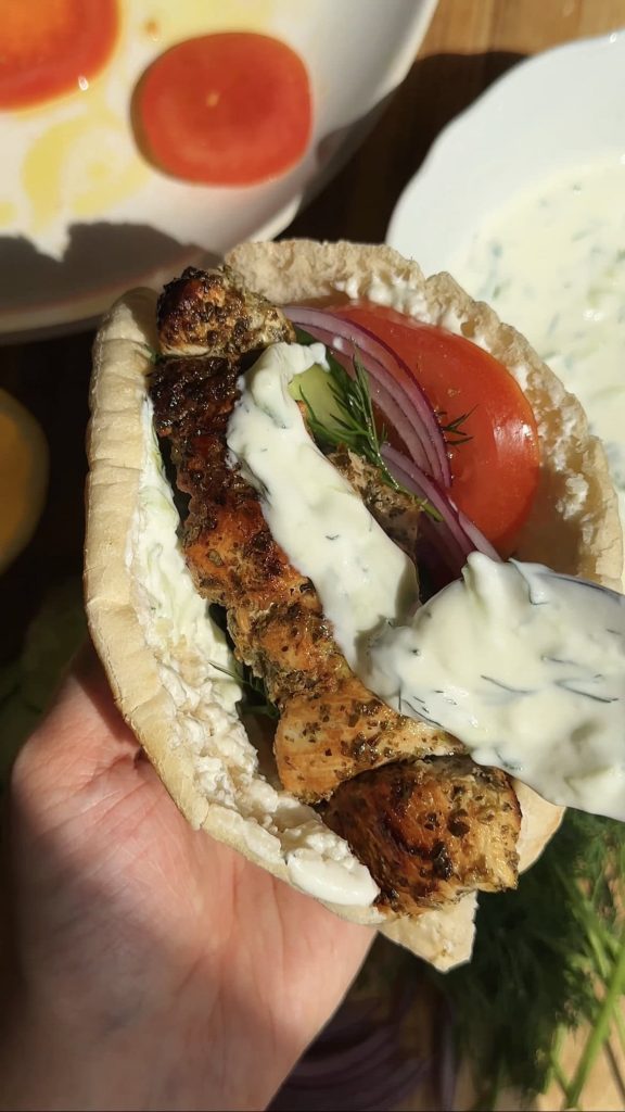 spooning tzatziki on chicken souvlaki pita