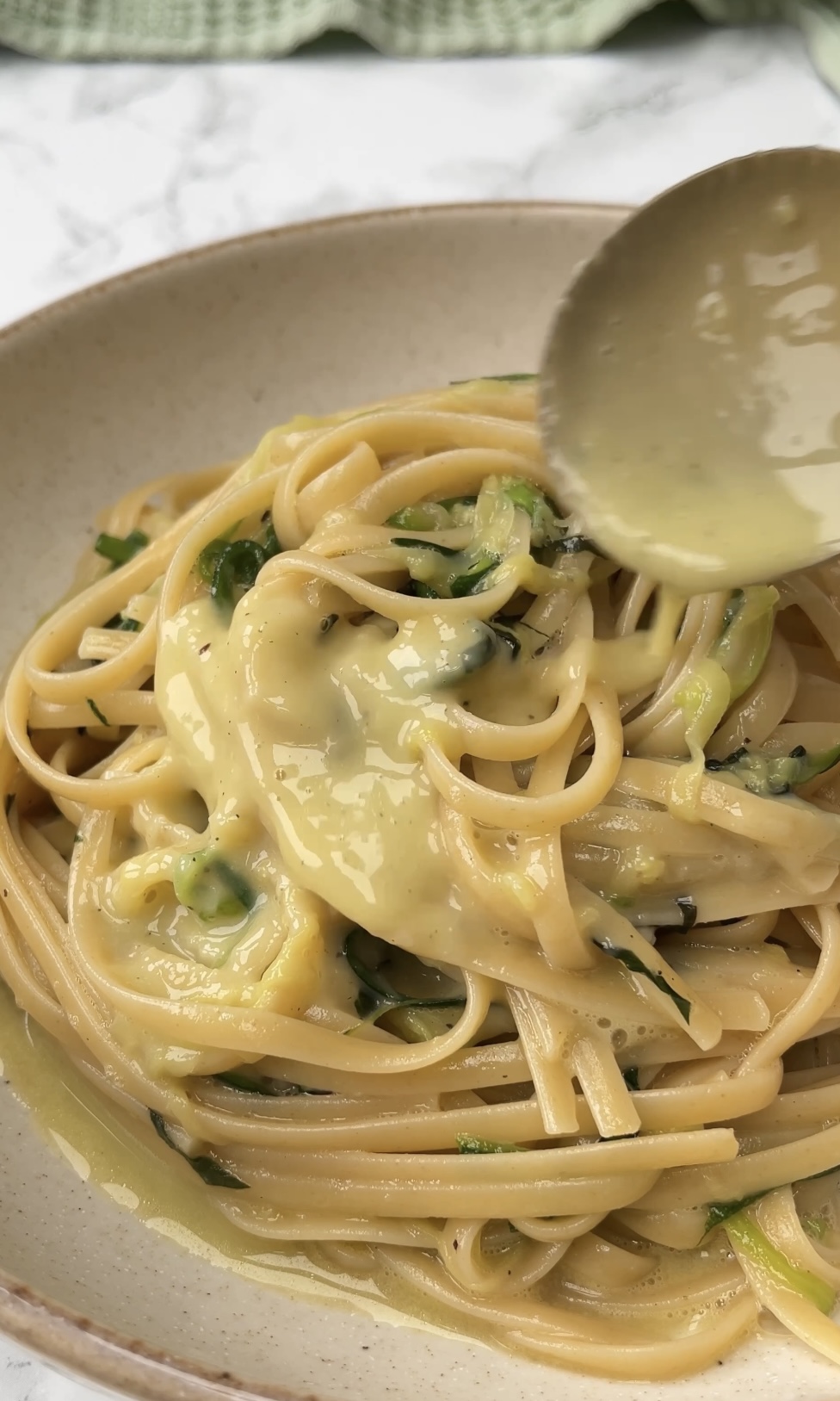 courgette carbonara pouring sauce over pasta.