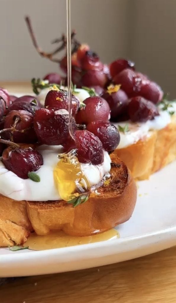 Drizzling honey on roasted grapes on ricotta toasts