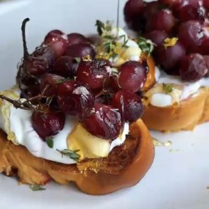 Drizzling honey on roasted grapes on ricotta toasts