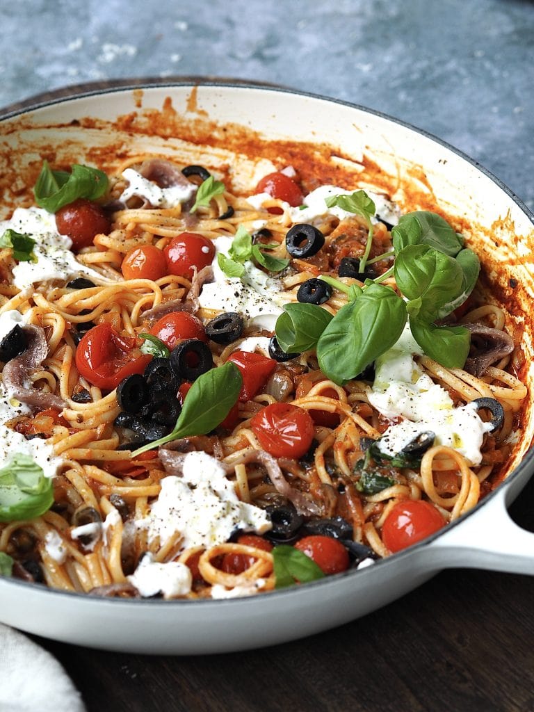 Puttanesca in a shallow casserole dish topped with torn burrata and fresh basil.