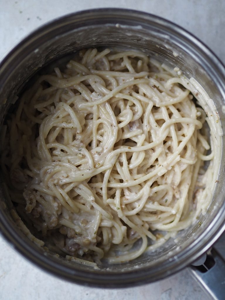 Close up of a saucepan of spaghetti with white pesto stirred through.