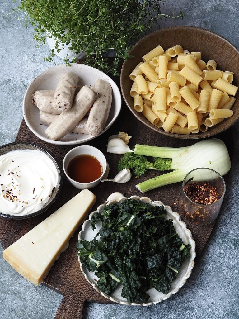 Ingredients to make Creamy Sausage and Fennel Rigatoni on a wooden board.