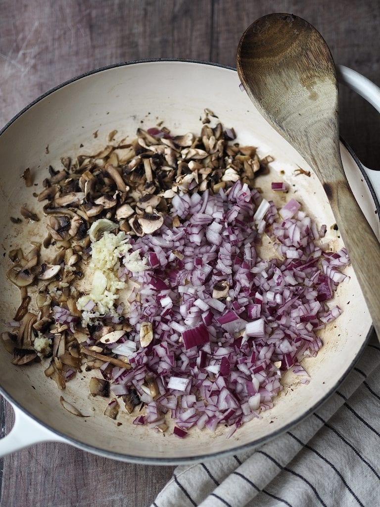 chopped red onion, mushrooms and garlic being fried in a shallow casserole dish.