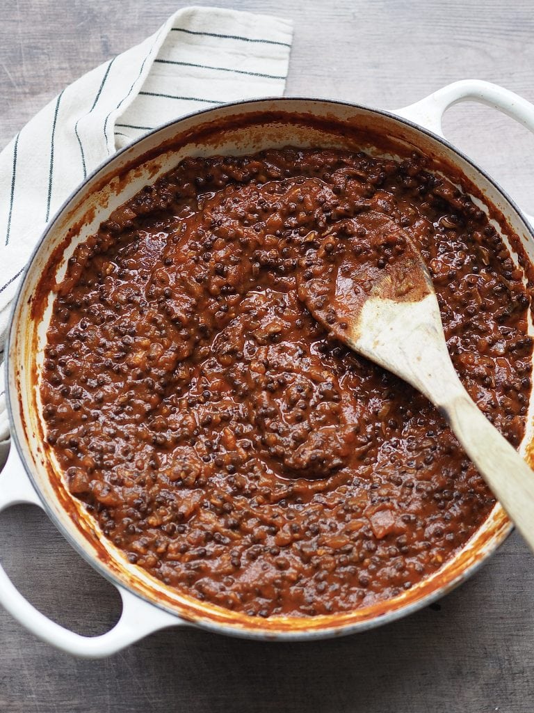 Lentil bolognese being stirred in a shallow casserole dish. 