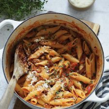 Penne with sausage ragu and grated cheese in a white casserole dish.