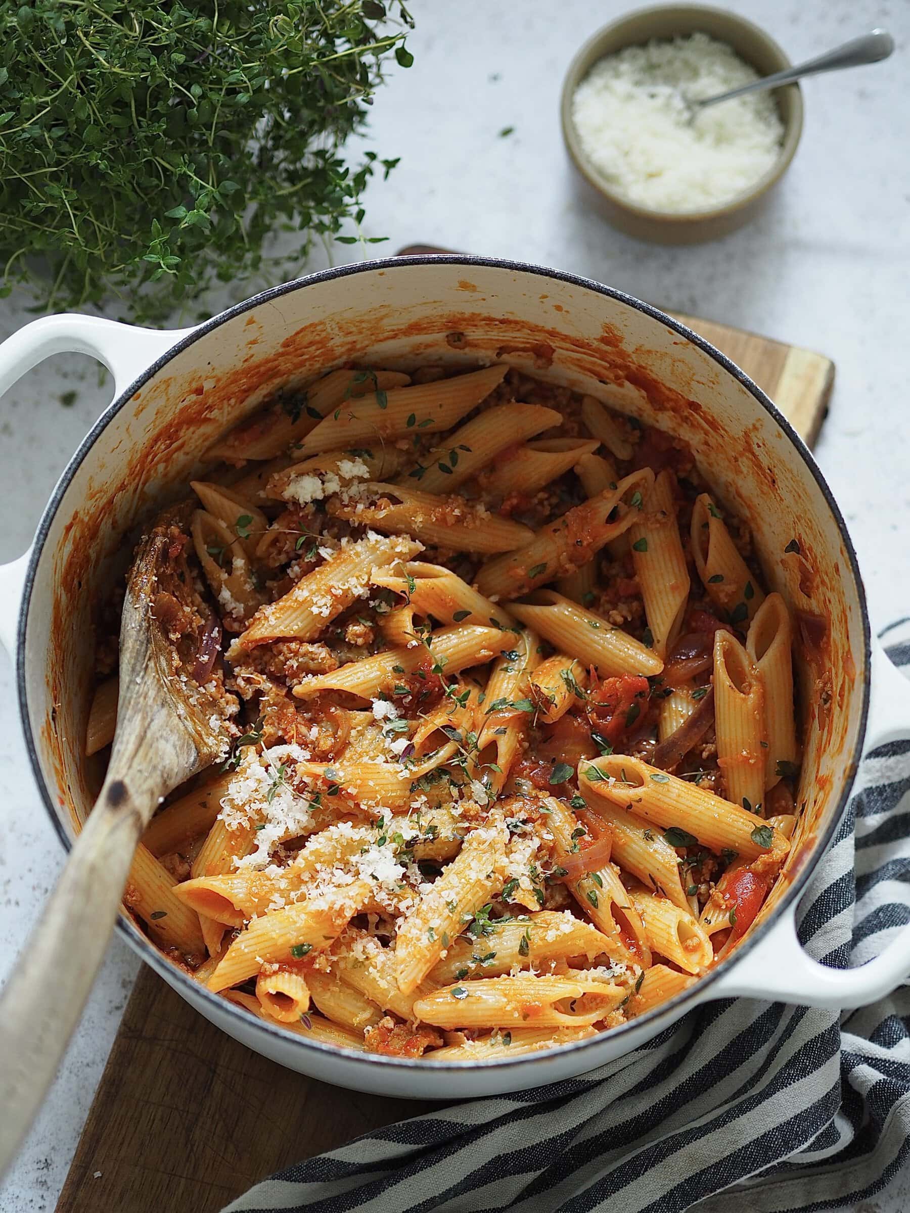 Penne with sausage ragu and grated cheese in a white casserole dish.
