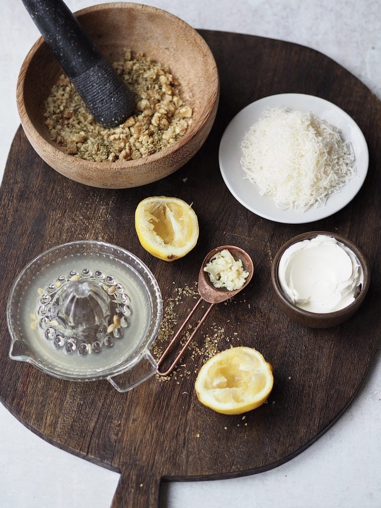 Ingredients to make white pesto displayed on a wooden board.