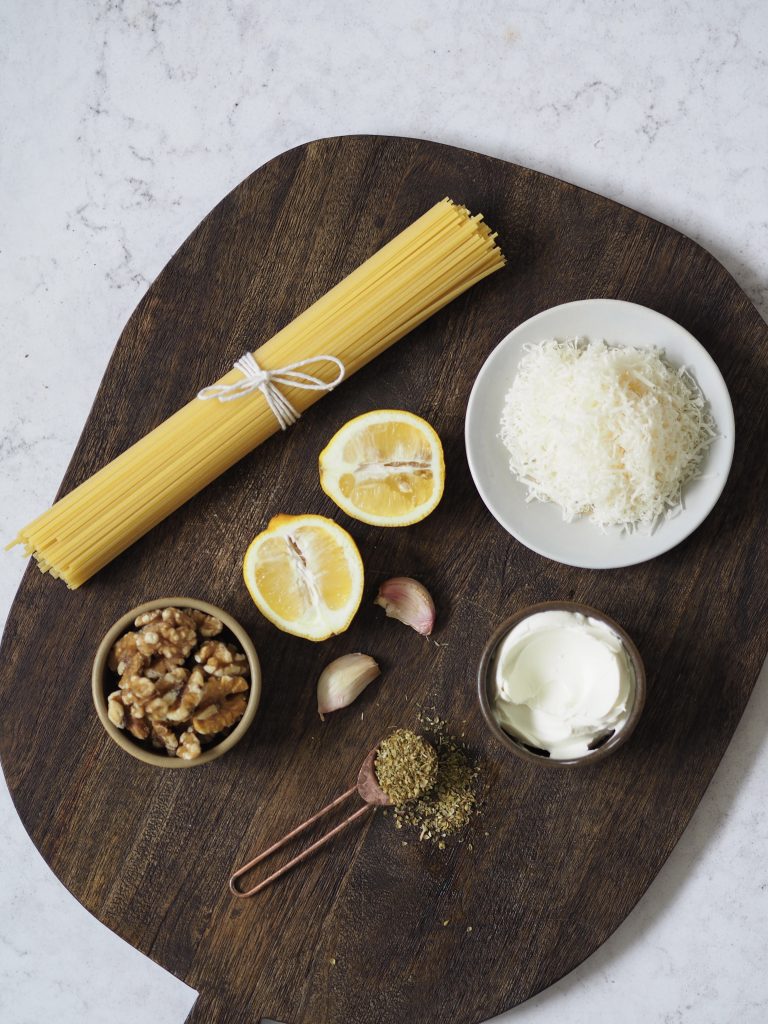 Ingredients to make white pesto pasta on a wooden board.