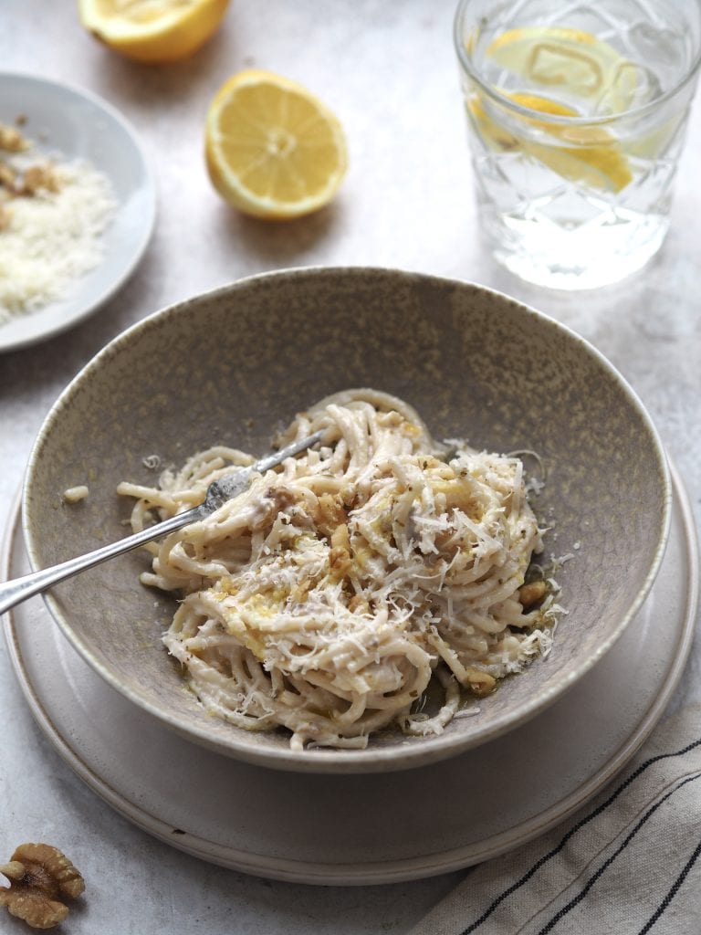 Grey bowl of white pesto pasta topped with grated cheese and crushed walnuts.