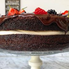 Side angle of moist chocolate cake filled with cream and topped with berries and ganache