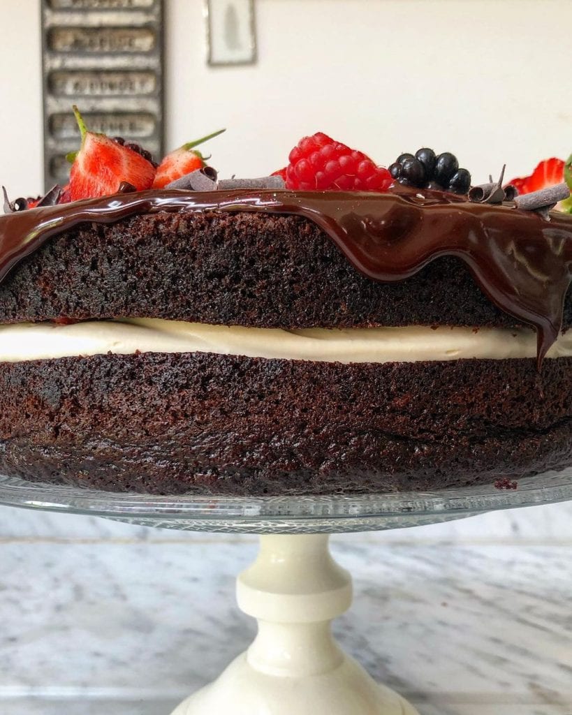 Side angle of moist chocolate cake filled with cream and topped with berries and ganache