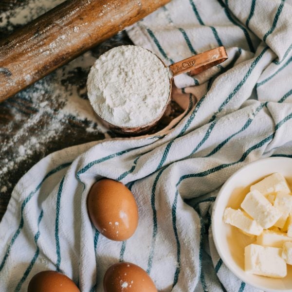 a photo of eggs, a cup of flour and softened butter on a tea towel