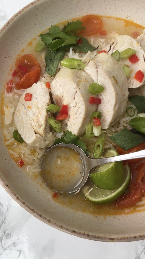 Spoon in the broth of Thai Chicken Soup With Rice in a beige bowl