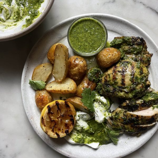 Zingy Grilled Chimichurri Chicken with Roasted Potatoes on a grey plate with a bowl of chimichurri yoghurt behind