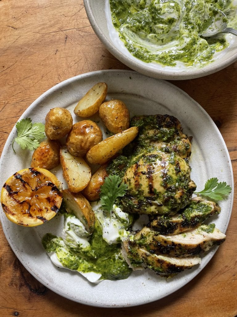 Zingy Grilled Chimichurri Chicken with Roasted Potatoes on a grey plate with a bowl of chimichurri yoghurt behind