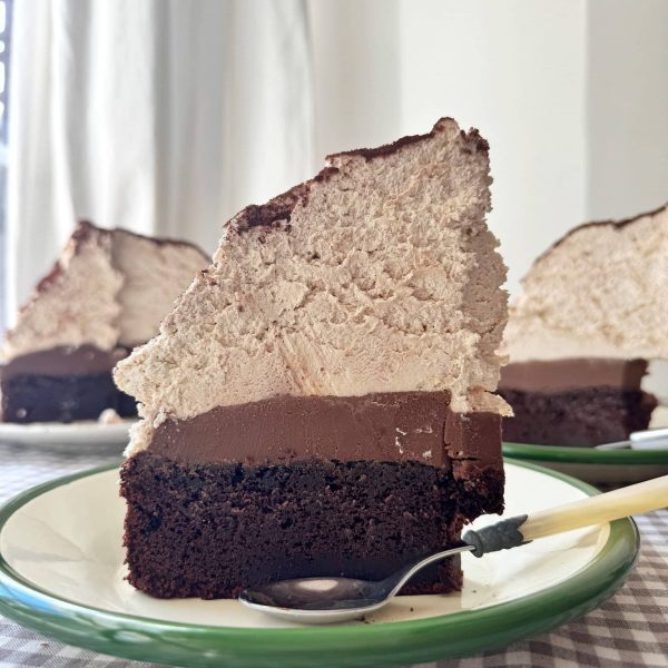 slice of chocolate mud cake with malted whipped cream stood on a green plate