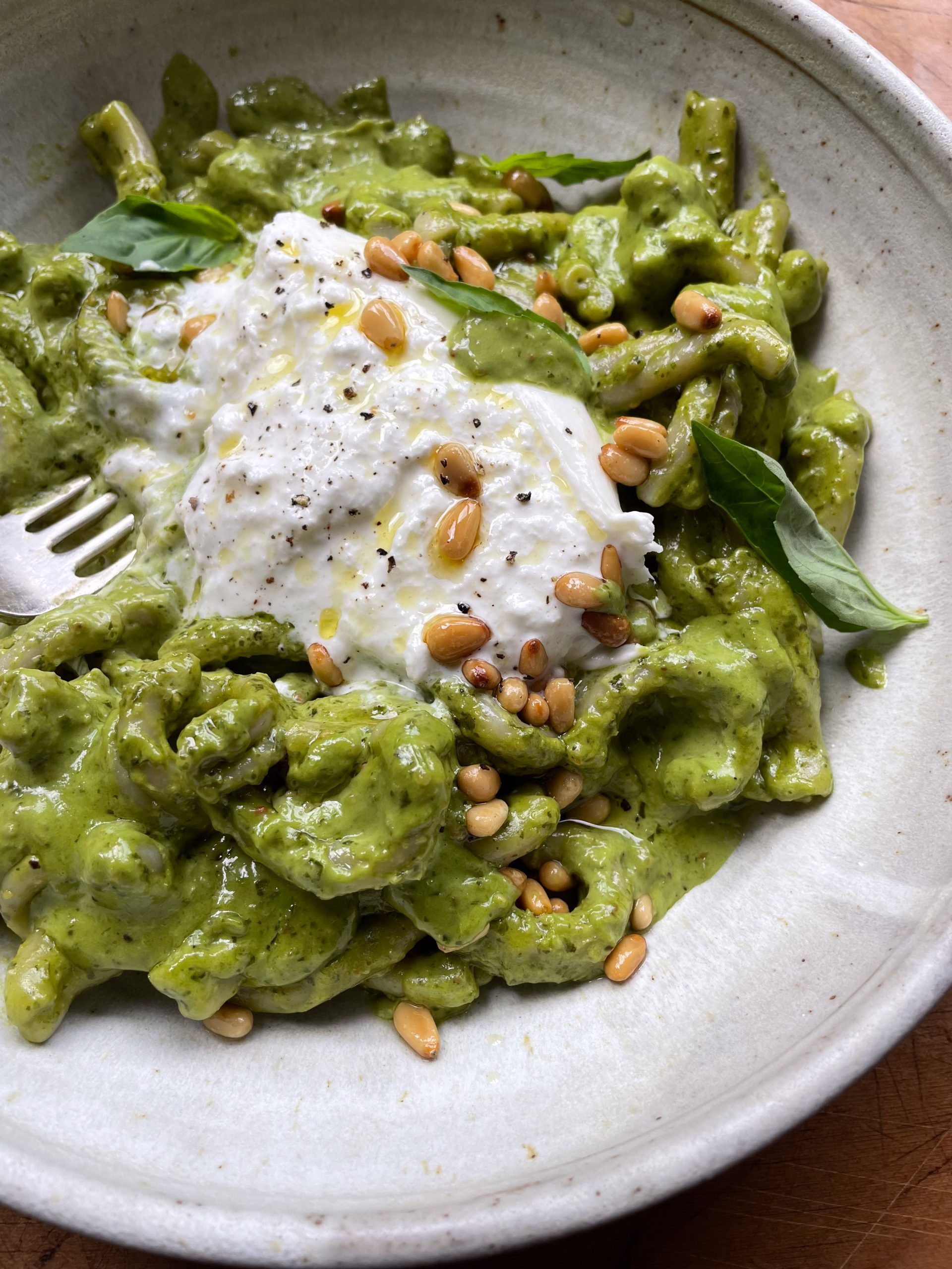 Close up of a bowl of creamy pesto pasta topped with toasted pine nuts.