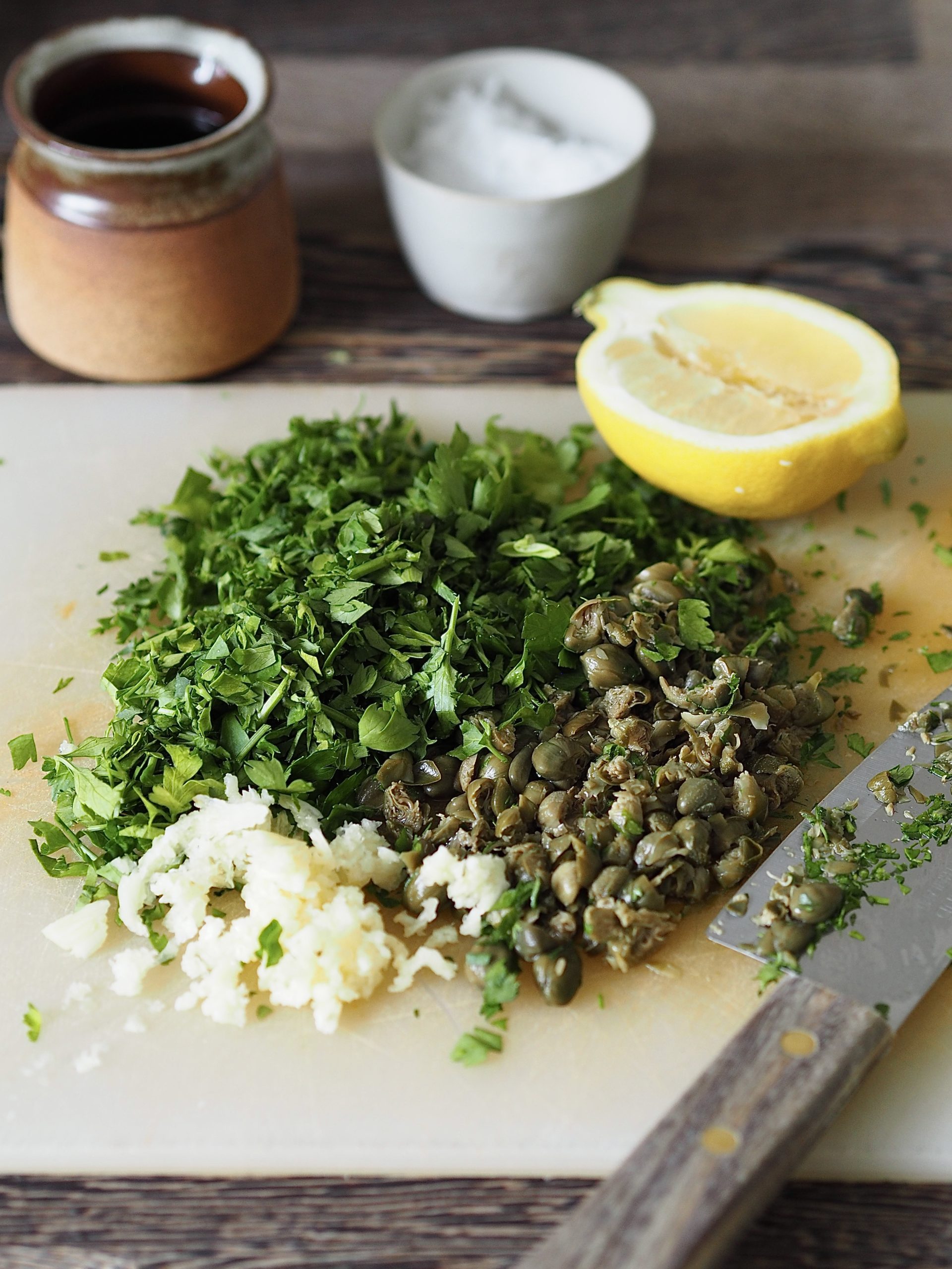 Chopped ingredients to make salsa verde on a cutting board.