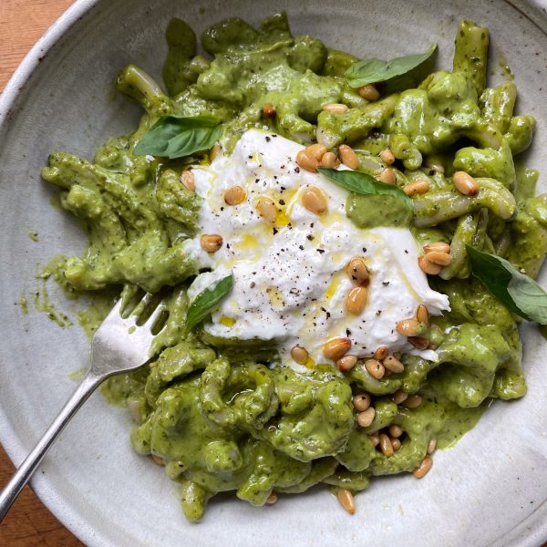 Stone bowl of pesto pasta with burrata and toasted pine nuts.