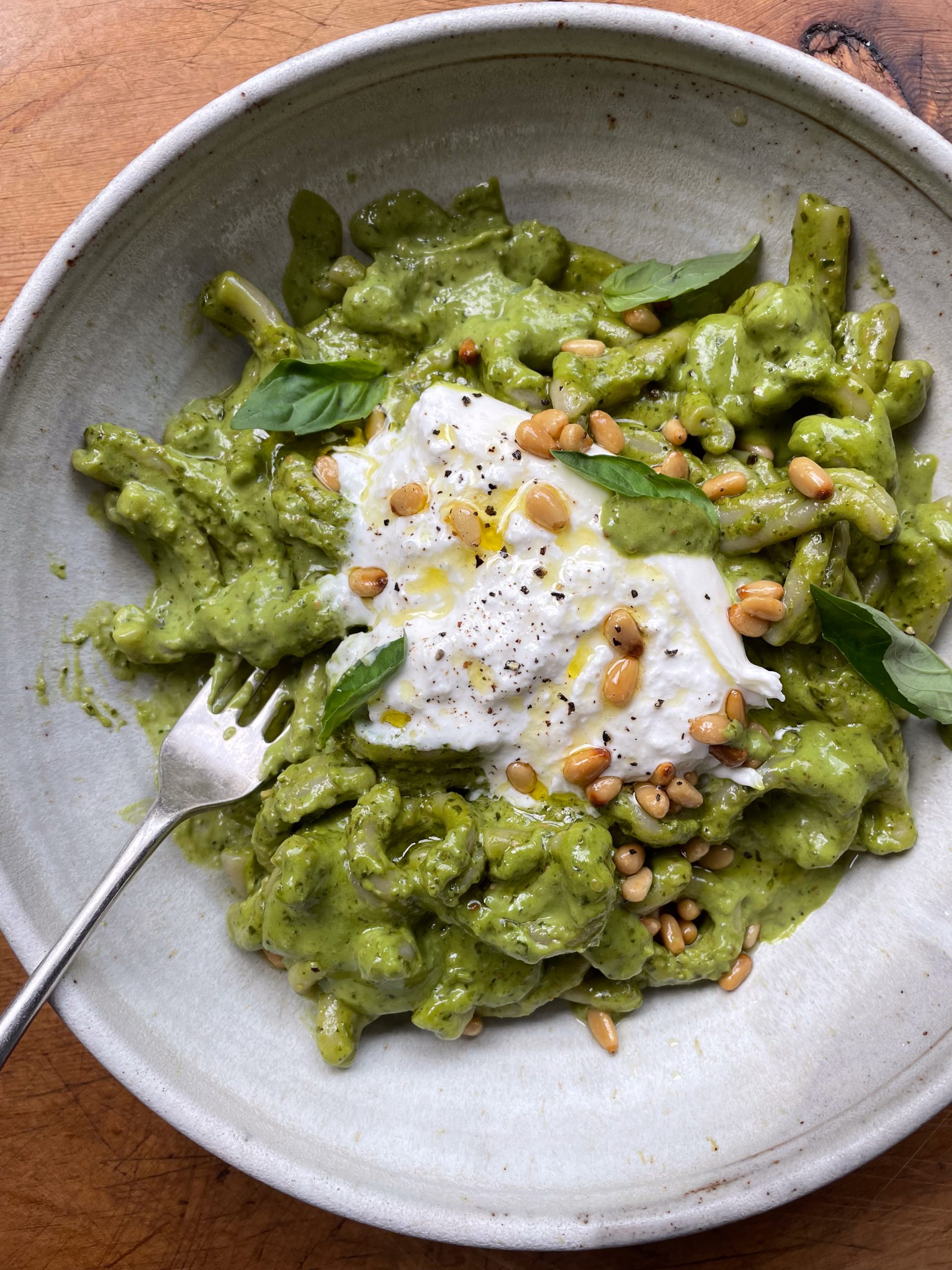 Stone bowl of pesto pasta with burrata and toasted pine nuts.