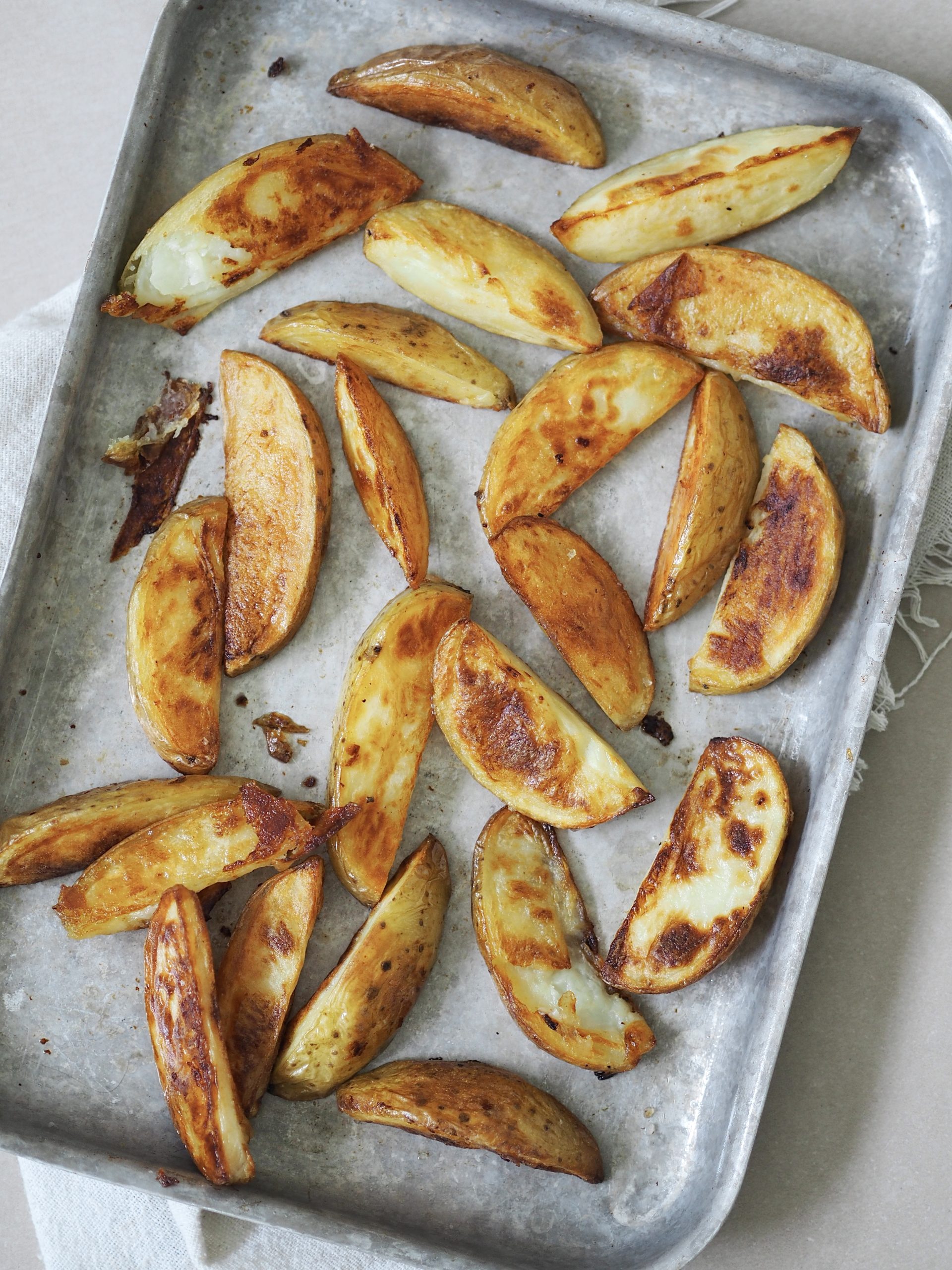 Crispy roasted potato wedges on a metal baking tray.