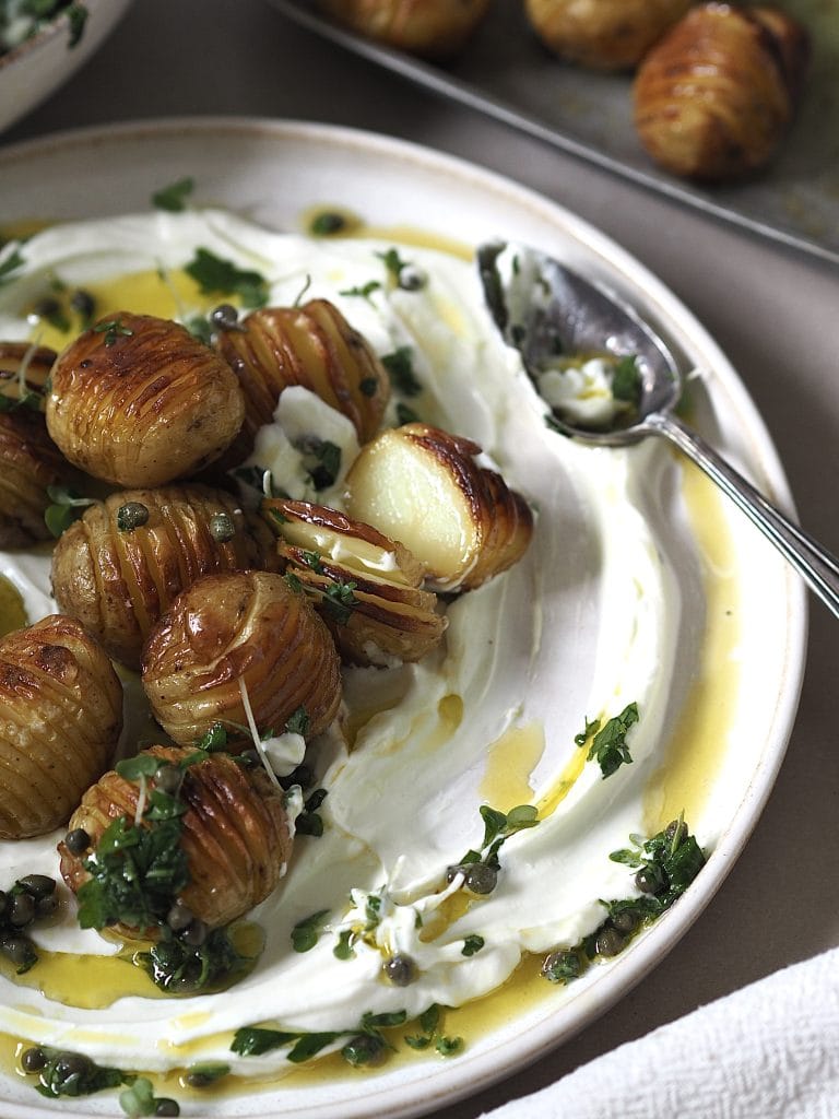 Close up of hasselbacked new potatoes on a plate of labneh.