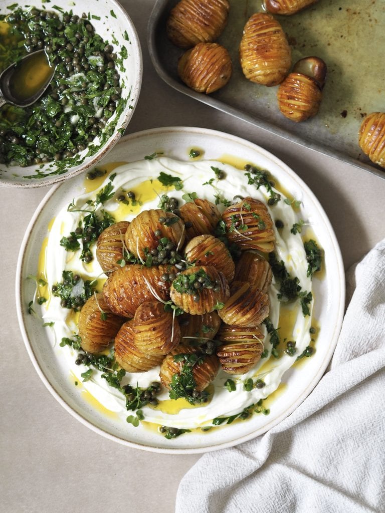 Grey plate of labneh topped with hasselback potatoes and salsa verde