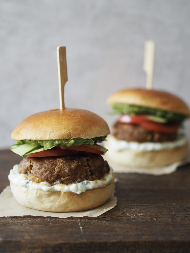 Two lamb burgers on a wooden worktop.