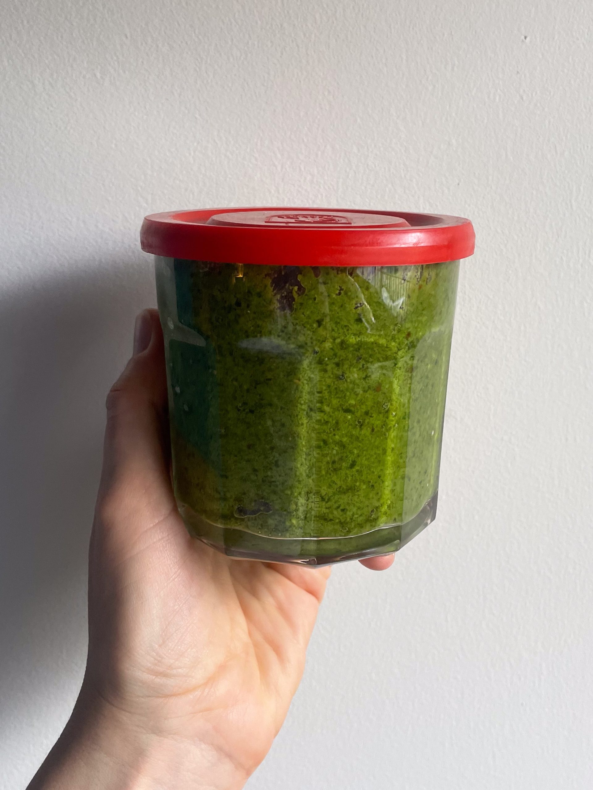 Hand holding a jar of pesto with a red lid.