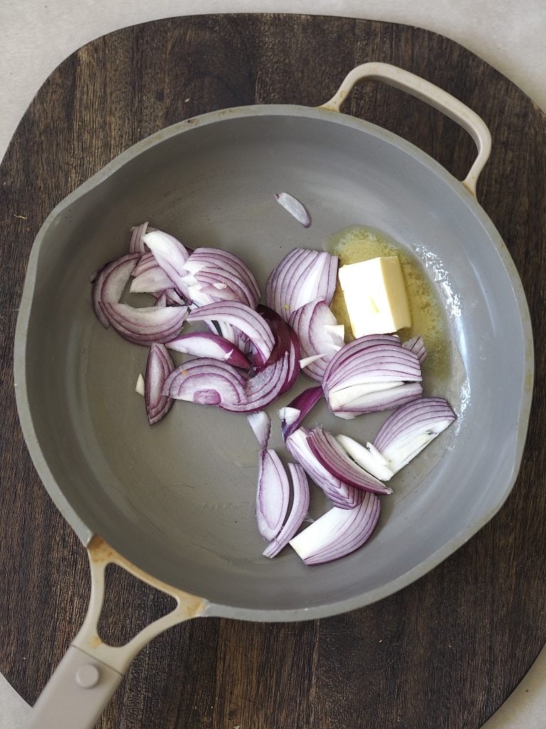 Raw red onions and butter in a frying pan.