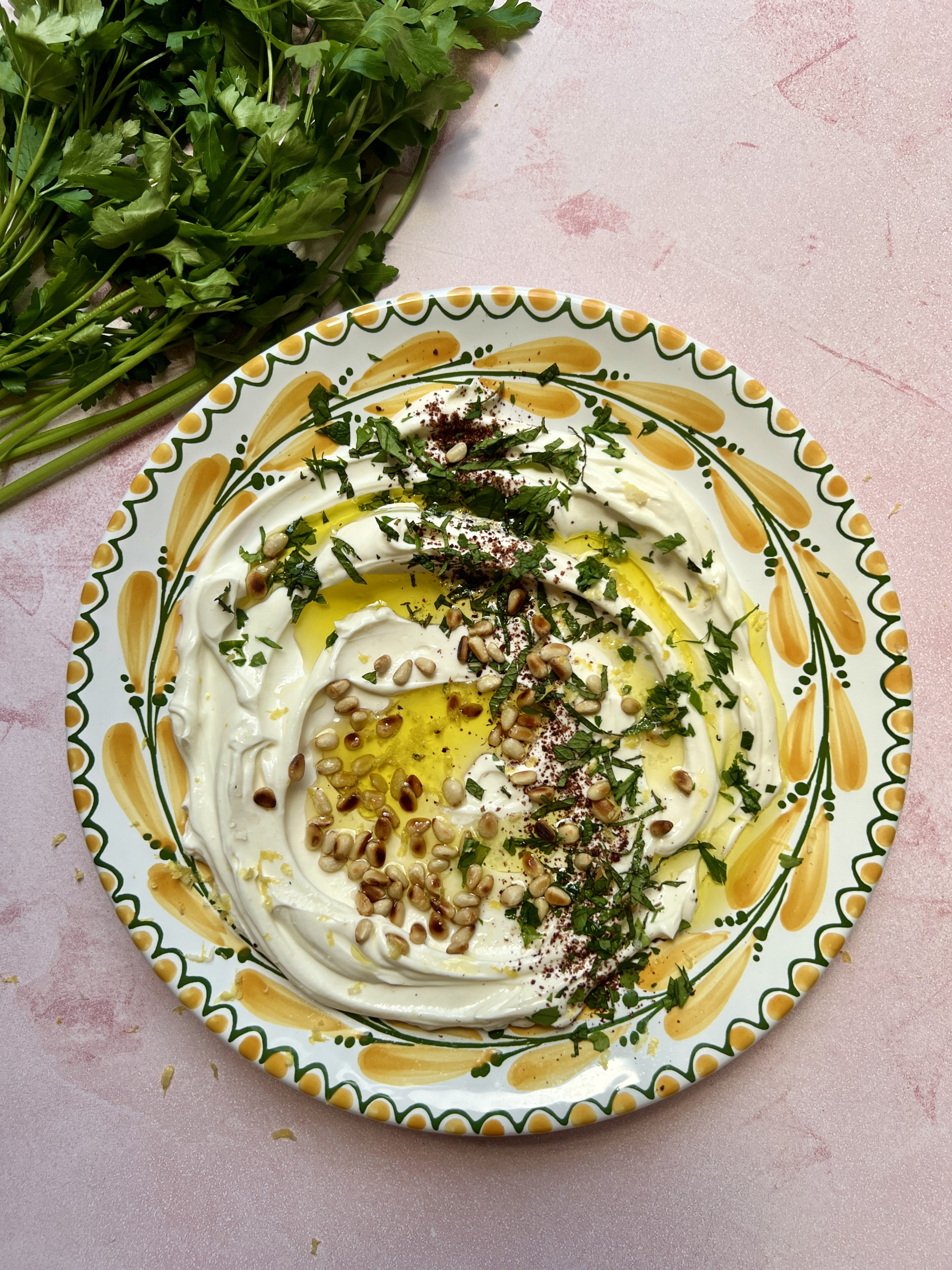 garlic labneh with pine nuts and parsley on a yellow and green plate