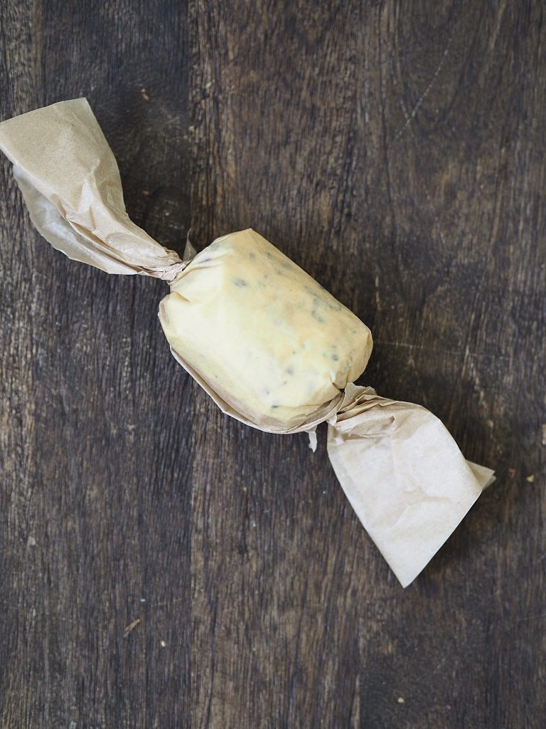 Compound butter wrapped in baking parchment on a wooden cutting board. 