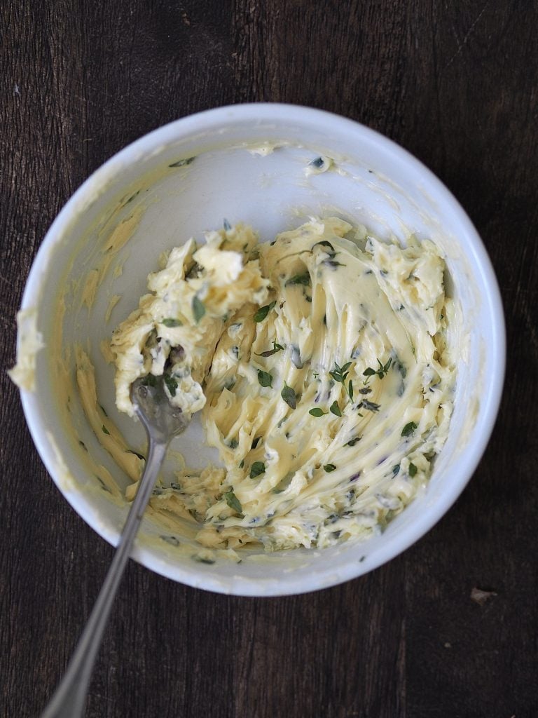 Garlic and thyme being beaten into soft butter with a fork.