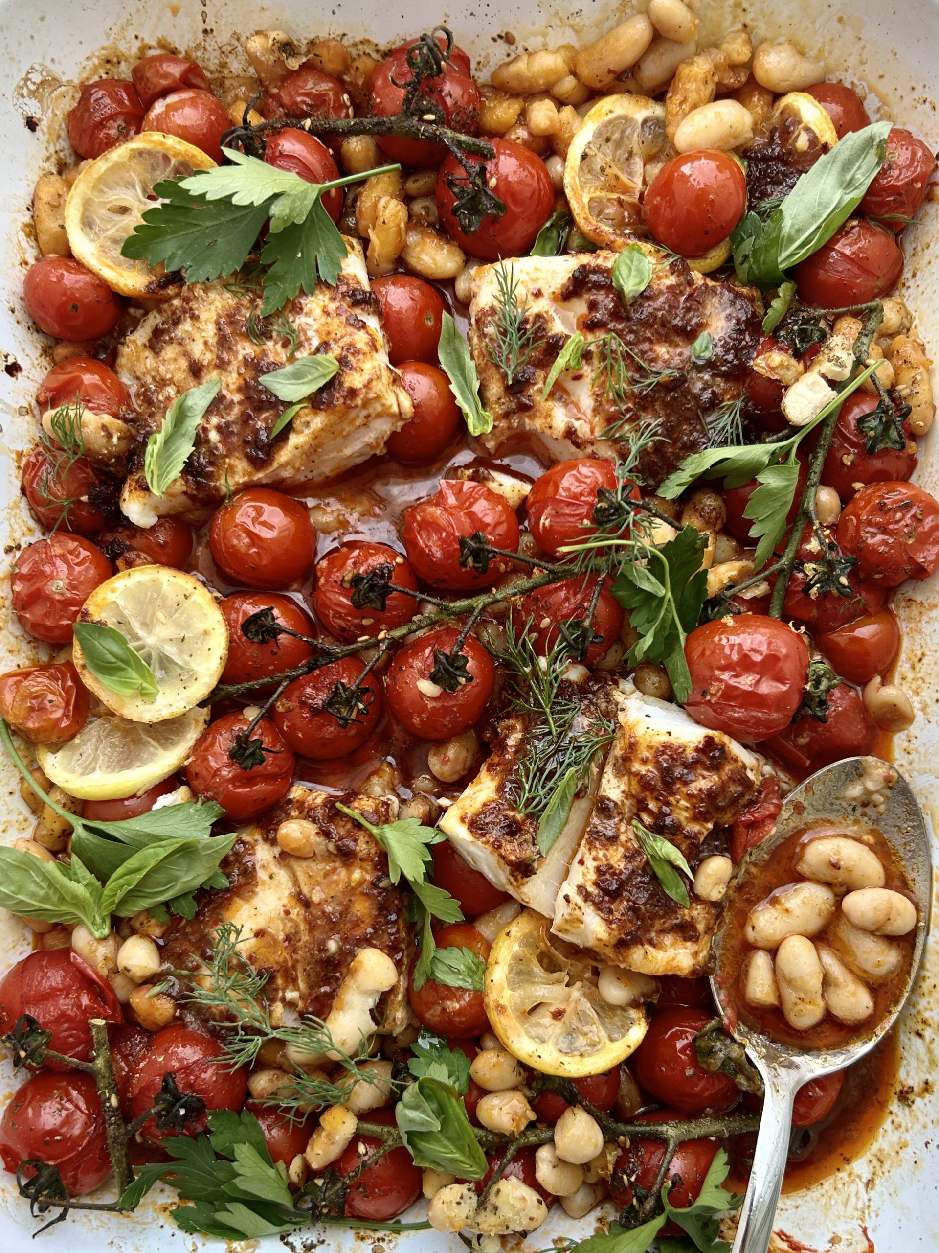 Close up of a traybake of harissa cod, cherry tomatoes, lemons and white beans.