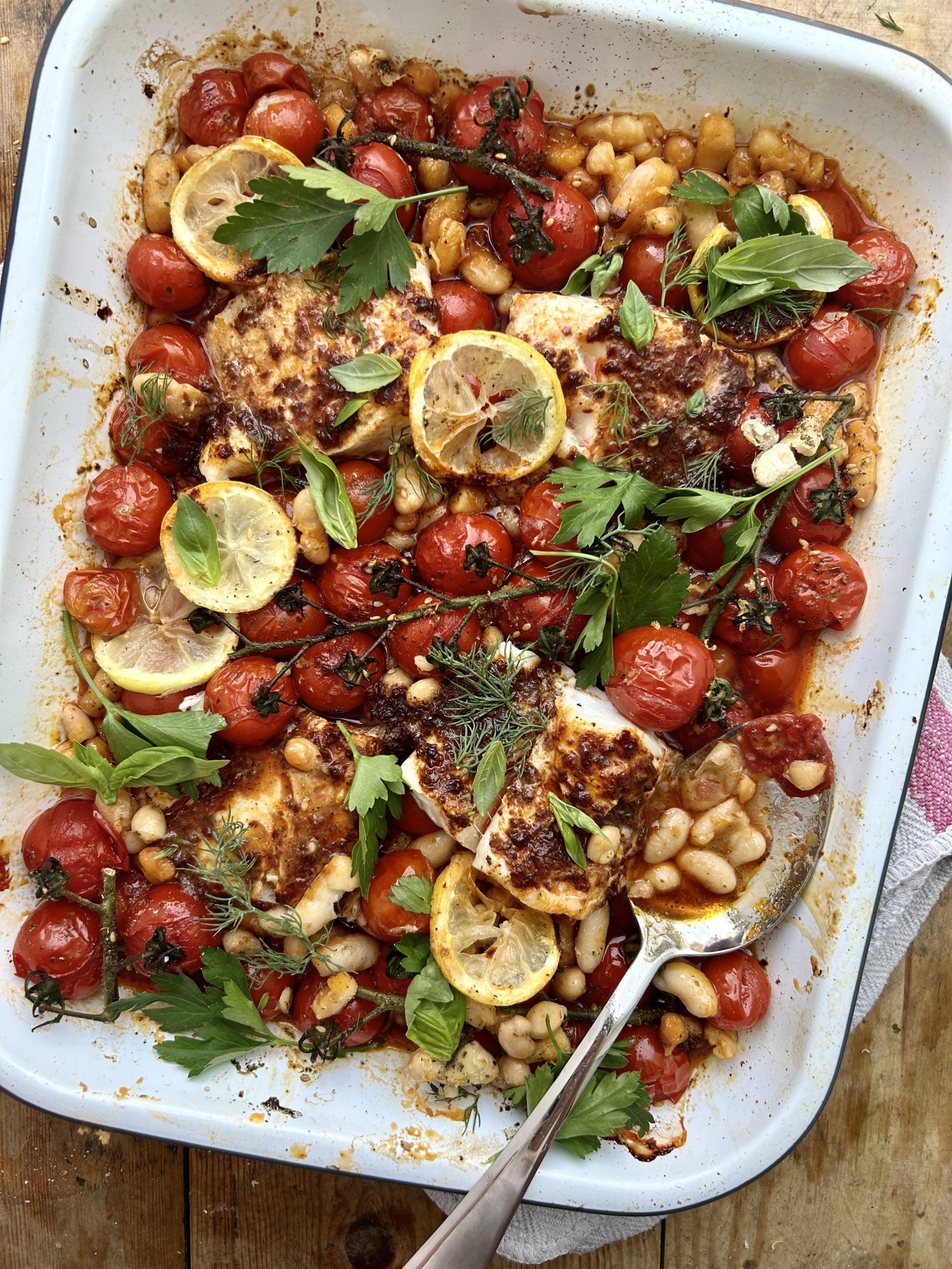 White tray of roasted tomatoes, beans and harissa cod.