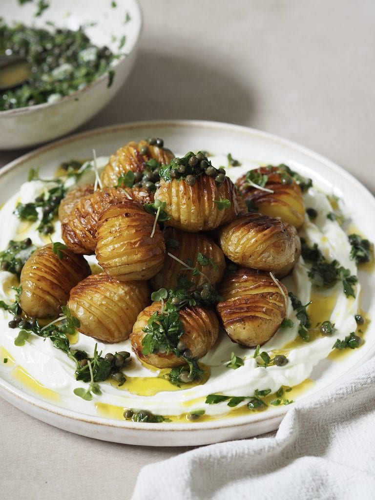 Plate of labneh and hasselback potatoes drizzled with salsa verde and finished with microgreens.