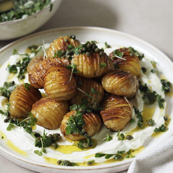 Plate of labneh and hasselback potatoes drizzled with salsa verde and finished with microgreens.