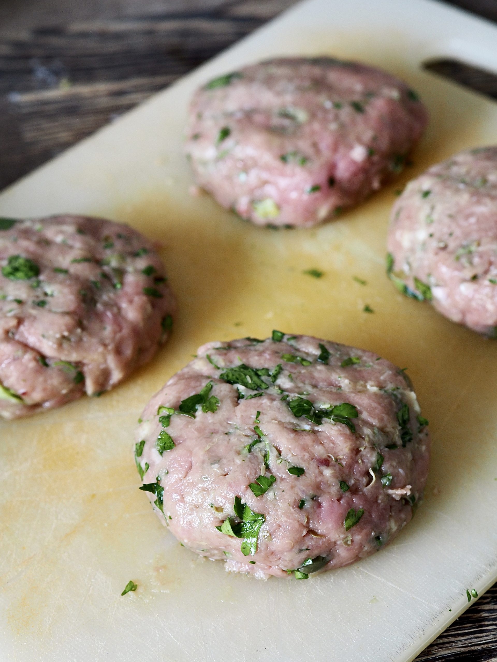 Shaped salsa verde chicken burgers on a white cutting board.